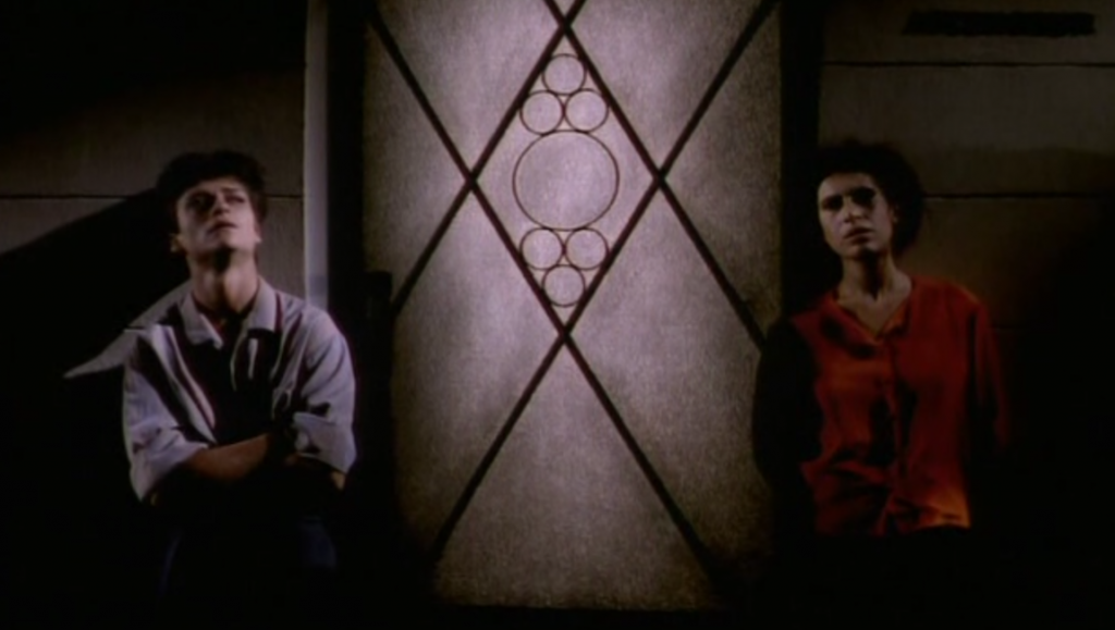 Night and Day | Chantal Akerman Night and Day film still. Two women stand near a geometric patterned wall.