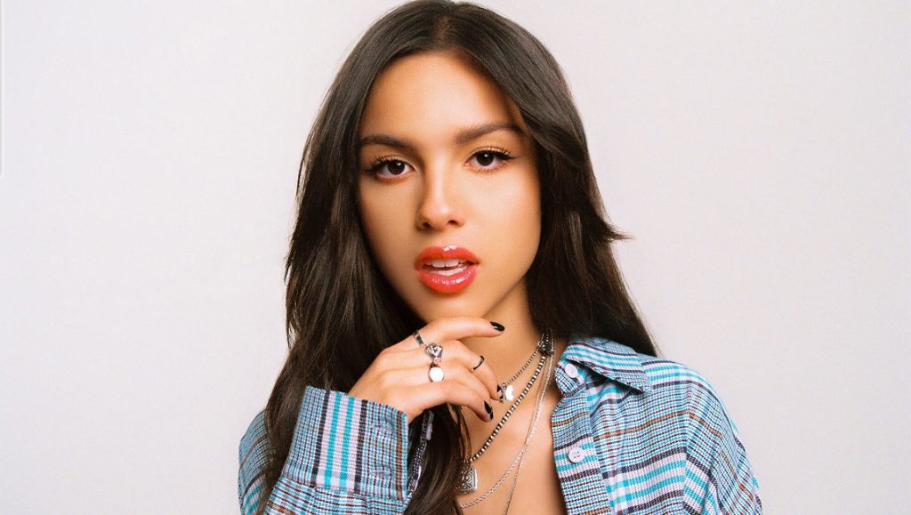 Olivia Rodrigo, Top Albums of 2021. Portrait of the singer wearing a plaid shirt and jewelry.