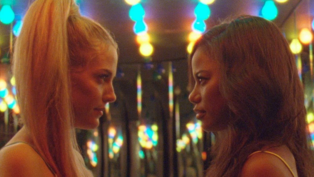 Zola | Janicza Bravo Zola movie scene. Two women face each other, with colorful lights in the background.