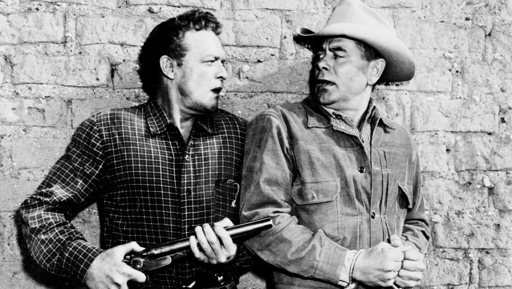 3:10 to Yuma movie still. Van Heflin guards Glenn Ford. Black and white western film.