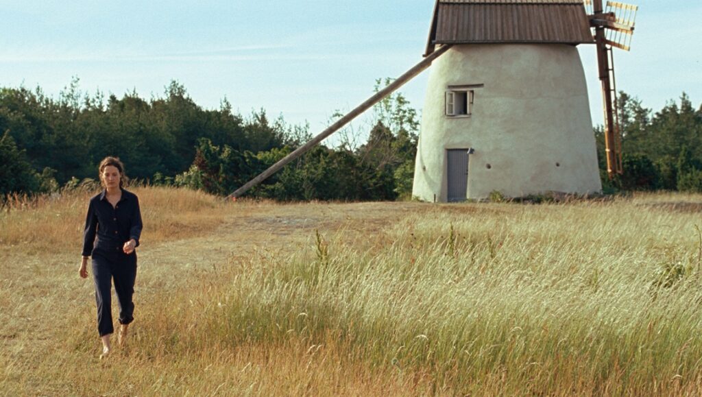 Still from Bergman Island at Cannes Film Festival 2021. Woman walks in field toward windmill.