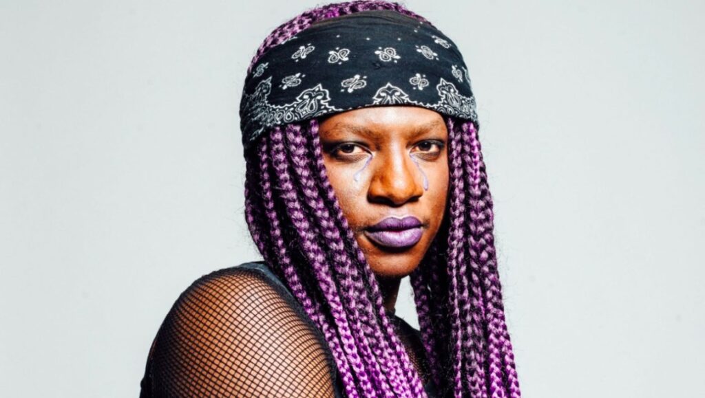 Backxwash | I Lie Here Buried with My Rings and My Dresses Backxwash, June 2021 album roundup. Rapper with purple braids and bandana.