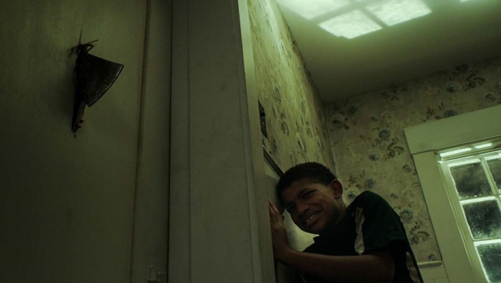 The Boy Behind the Door | David Charbonier & Justin Powell The Boy Behind the Door movie scene. Scared boy by a door, axe in the wall. Horror film.