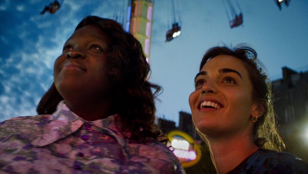 The Braves film still: Two women smiling, looking up at a carnival ride.