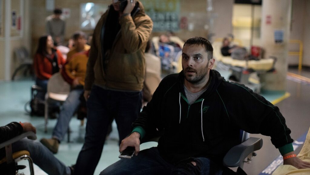 La Fracture | Catherine Corsini La Fracture film still from Cannes Film Festival 2021. Man in wheelchair with shocked expression in a busy hospital waiting room.
