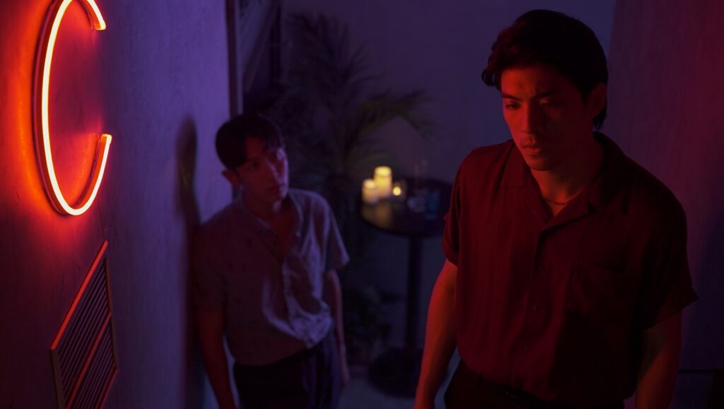 Cannes Film Festival 2021 — Dispatch 3: Moneyboys, A Radiant Girl, Medusa Two men in a dimly lit room with neon light. Nightlife scene with a modern aesthetic. Interior with a bar table and candles.