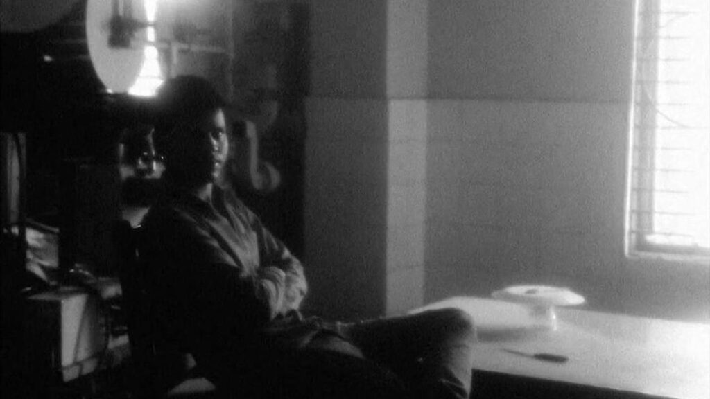 Night of Knowing film still from Cannes Film Festival 2021. Man sitting in a chair. Black and white.