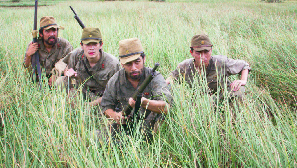 Four Japanese soldiers with rifles hide in tall grass. World War II movie scene.
