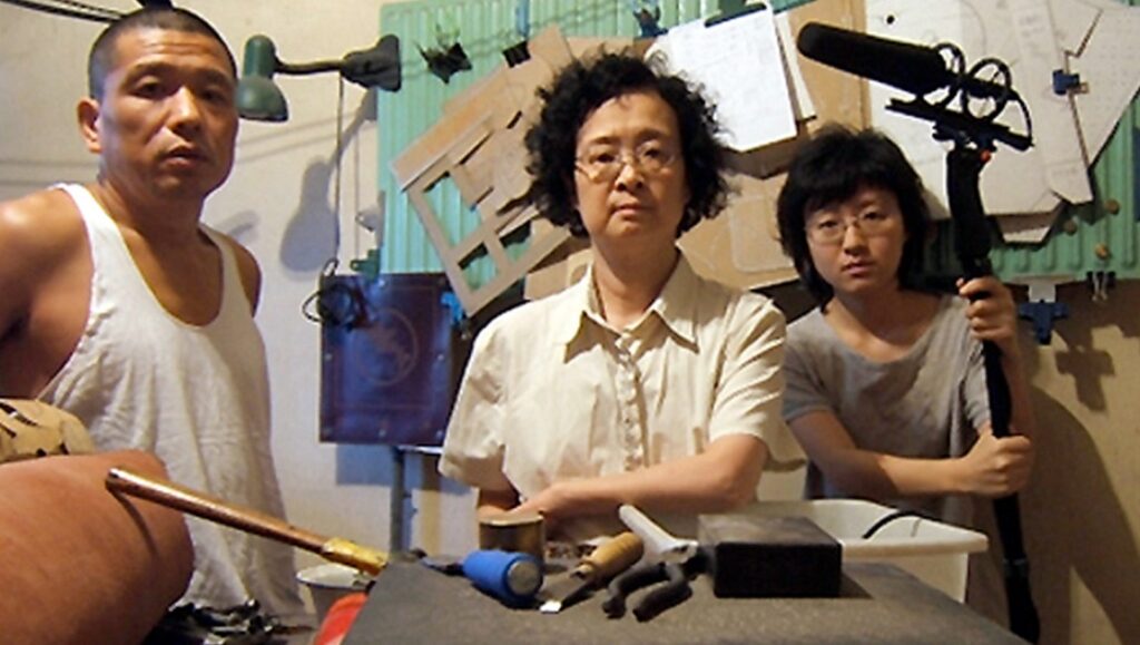 Oxhide film still: Liu Jiayin's family in a cramped space. Mother, father, and daughter with film equipment.