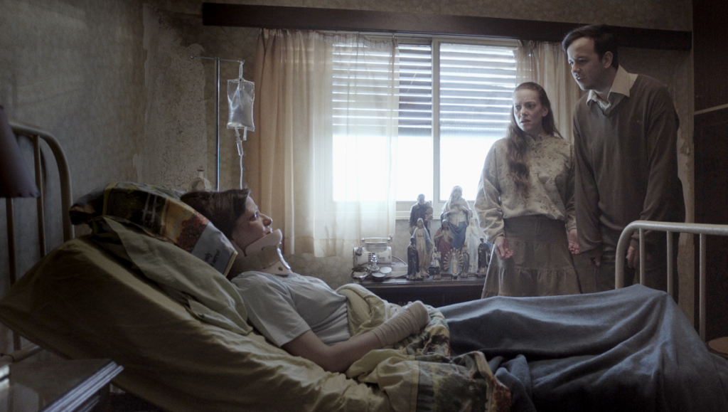 Before We Vanish film still: Woman in hospital bed with visitors. Religious figurines nearby. July 2021 movie review.