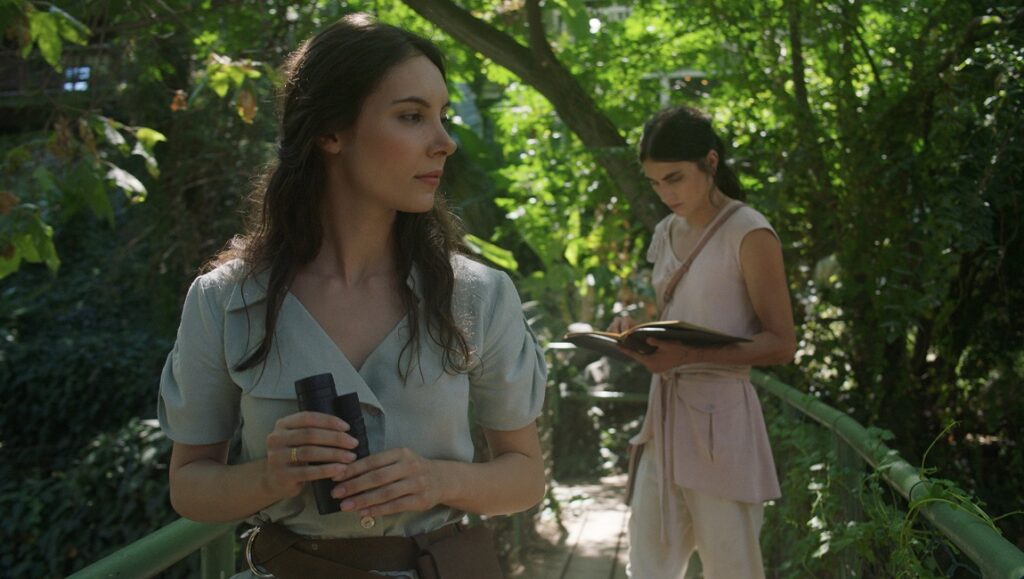 Topology of Sirens film still. Two women in nature, one holds binoculars, the other a notebook. FIDMarseilles 2021.