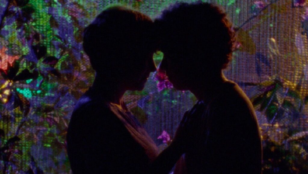 Tsugua Diaries at Cannes Film Festival: Two figures in silhouette, face to face, against a colorful, abstract background.