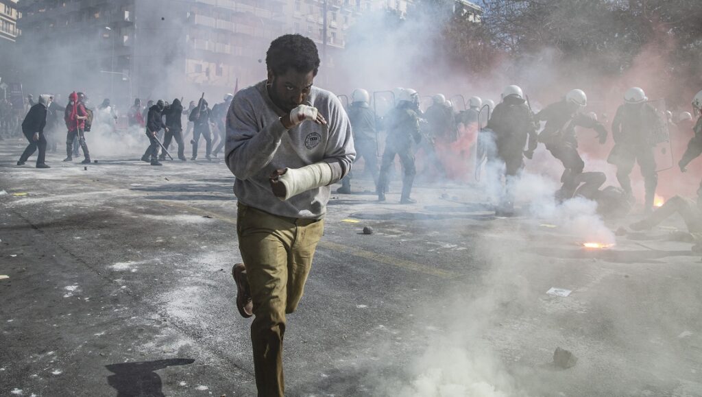 Locarno Film Festival 2021 — Dispatch 1: Beckett, Respect, Zeroes and Ones Beckett movie scene: Man with arm cast runs from riot police in smoke-filled street. Ferdinando Cito Filomarino film.