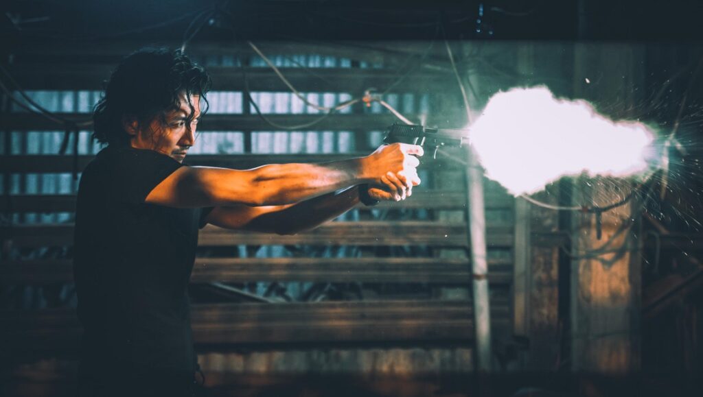 Nicholas Tse in Raging Fire, NYAFF 2021. Man firing a gun, muzzle flash visible. Action film scene.