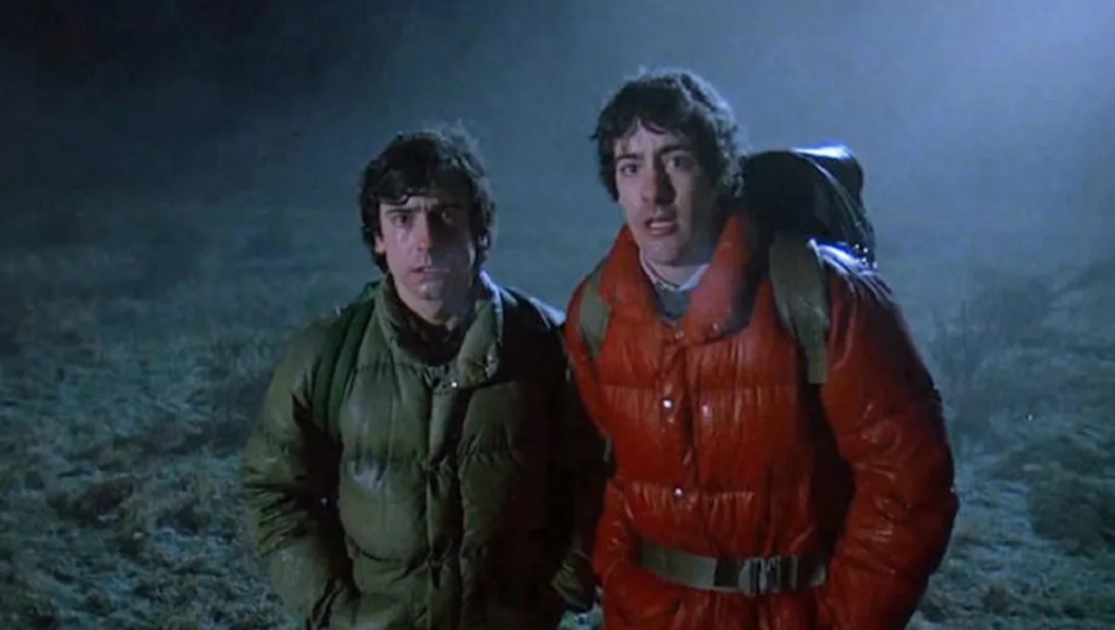 American Werewolf in London film still. Two men in puffer jackets look concerned in a foggy, dark landscape. Horror movie.