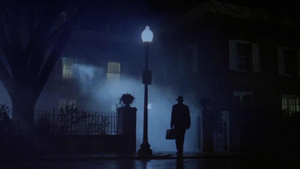 The Exorcist | William Friedkin The Exorcist movie scene. Man in hat with bag walks under streetlight at night. William Friedkin film.