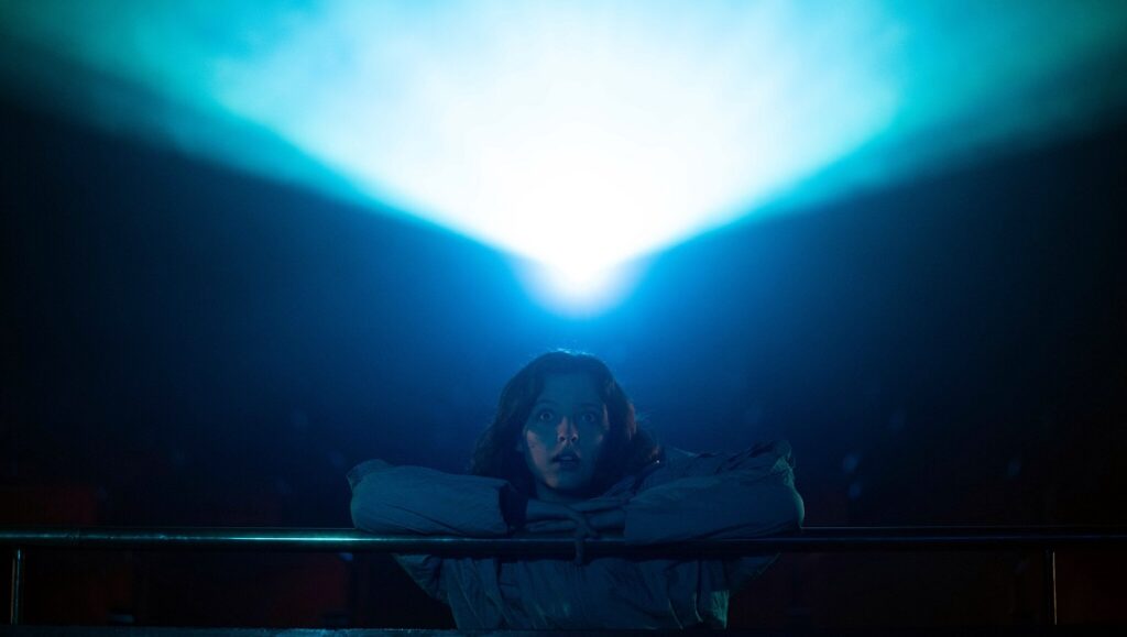 The Last Matinee movie scene. Woman in a dark theater with a bright projector beam. Horror film.