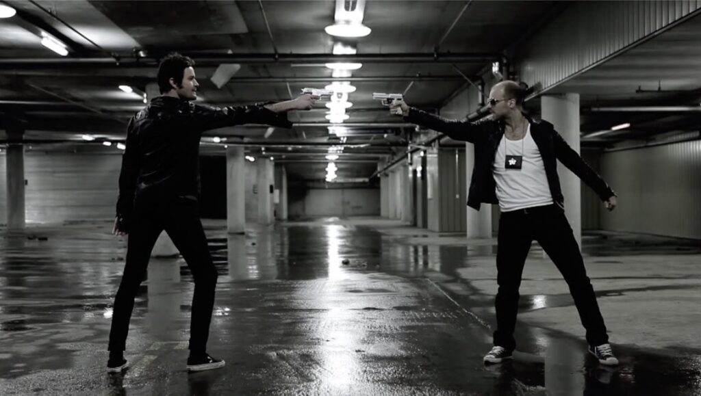 Zeroes and Ones film still from Locarno Film Festival. Two men point guns at each other in a parking garage.