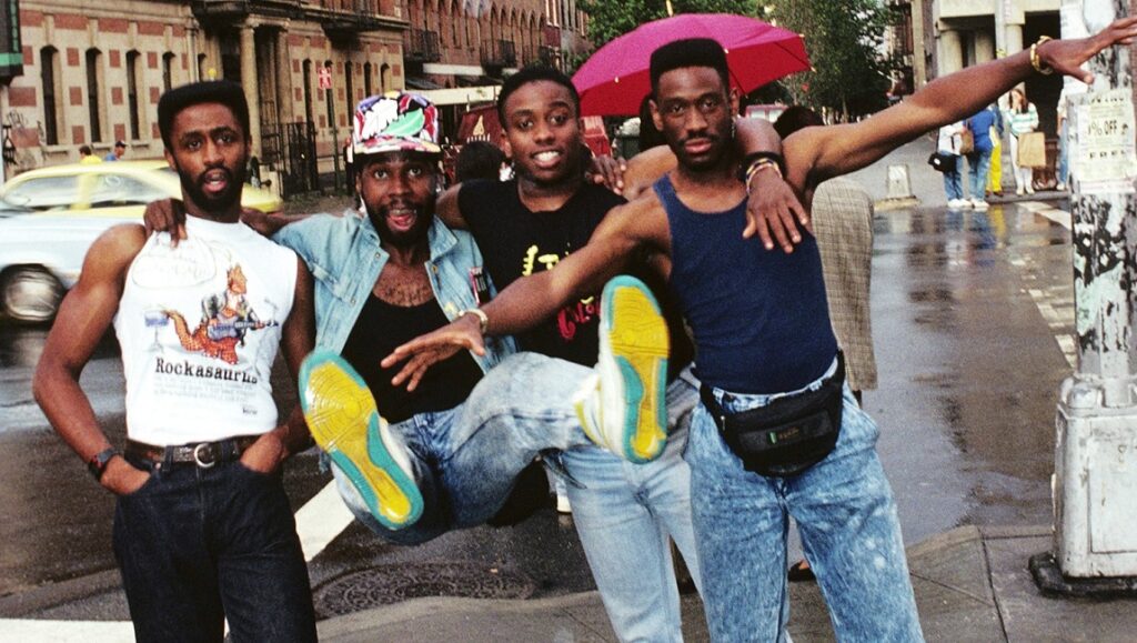 Living Colour band members, Vivid era. Group photo on a city street. 1980s or 1990s fashion.