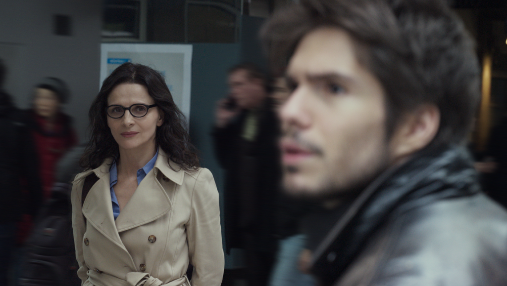 Who You Think I Am | Safy Nebbou Who You Think I Am movie still. Juliette Binoche in a trench coat and glasses, with a man in the foreground.