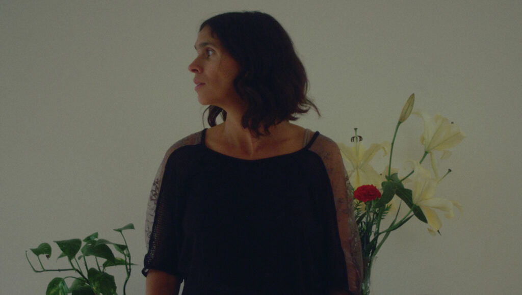 TIFF 2021 — Dispatch 7: The Wavelengths Shorts Still from Dear Chantal at TIFF 2021. Woman in black top with flowers and plant.