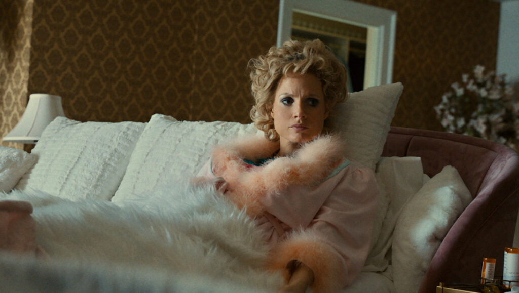 Jessica Chastain in The Eyes of Tammy Faye at TIFF 2021. Tammy Faye lounges in bed with a pink robe.