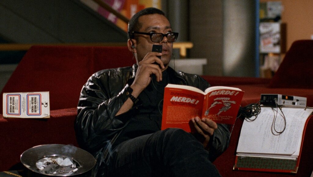 NYFF 2021: Still from Chameleon Street. Man reads a book titled Merde! while recording audio. Film review.