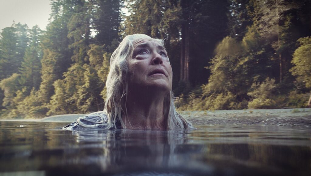 Freeland movie scene. Woman in river, looking up. Trees in background.
