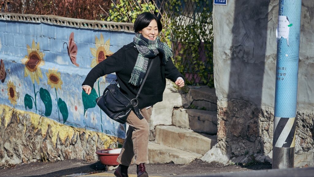 Lucky Chan-sil | Kim Cho-hee Kim Cho-hee's Lucky Chan-sil film still. A woman smiles, walking past a sunflower mural. Indie film.