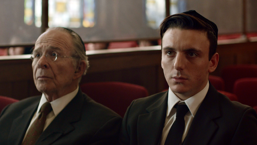 Minyan film scene: Two men wearing kippahs sit in a synagogue. October 2021 film.