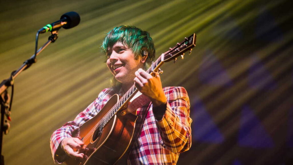 Billy Strings performing live in September 2021. Musician with green hair plays guitar and sings. Album Roundup.