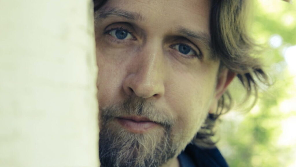Hayes Carll album cover. Singer-songwriter with beard, blue eyes, and long hair. October 2021 music roundup.