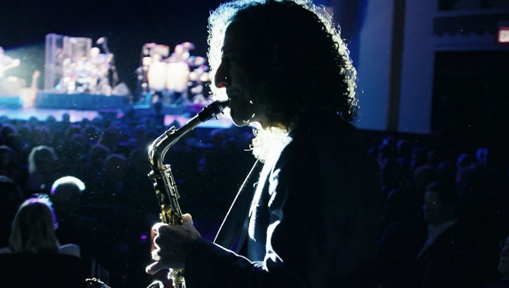 Kenny G performs at DOC NYC 2021. Musician plays saxophone on stage in front of a crowd.