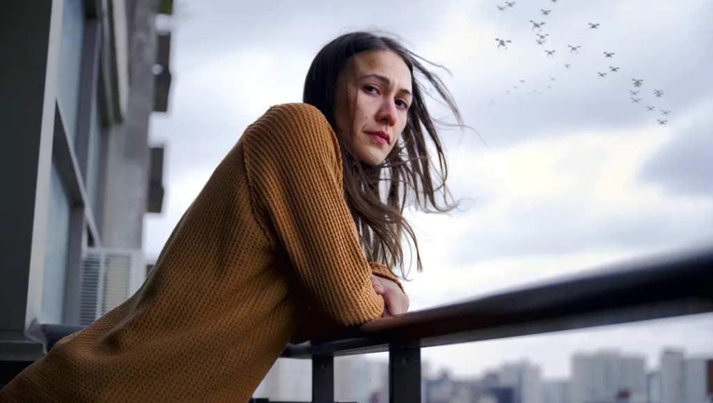 Night Raiders | Danis Goulet Night Raiders film still: Woman on balcony with drones in the sky. Dystopian future.