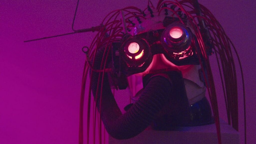 Michael M. Bilandic's Project Space 13: A futuristic mask with glowing eyes and red wires against a purple backdrop.