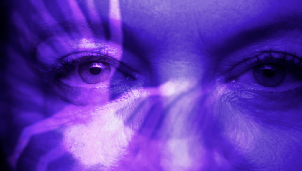 Brainwashed concept. Close-up of a woman's face, eyes, and purple light rays. Mind control.