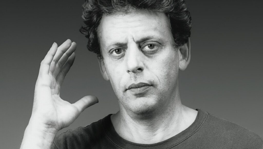 Philip Glass portrait. Composer of Glassworks with hand raised. Minimalist music icon.