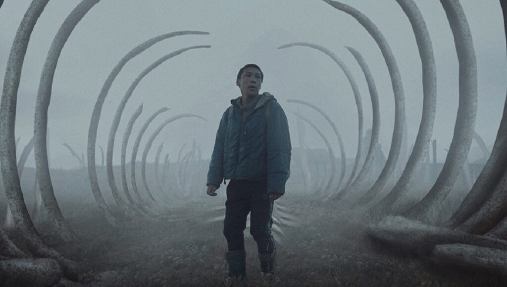 Philipp Yuryev's The Whaler Boy film still. Young man stands amidst whale bone arches in a misty landscape.