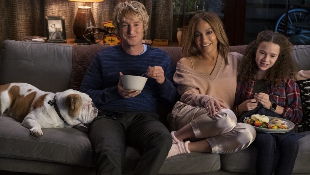 Marry Me — Kat Coiro Marry Me movie scene: Jennifer Lopez, Owen Wilson, and child actor on a couch with a dog.