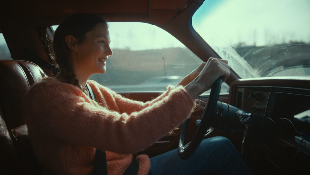 Film still from Hold Me Tight: Woman driving a car, smiling. IFFR movie review.