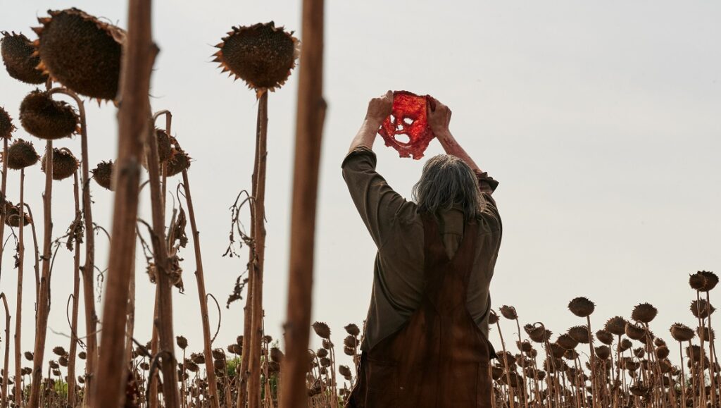 Texas Chainsaw Massacre — David Blue Garcia Leatherface holding a bloody mask in a sunflower field in Texas Chainsaw Massacre (2022).