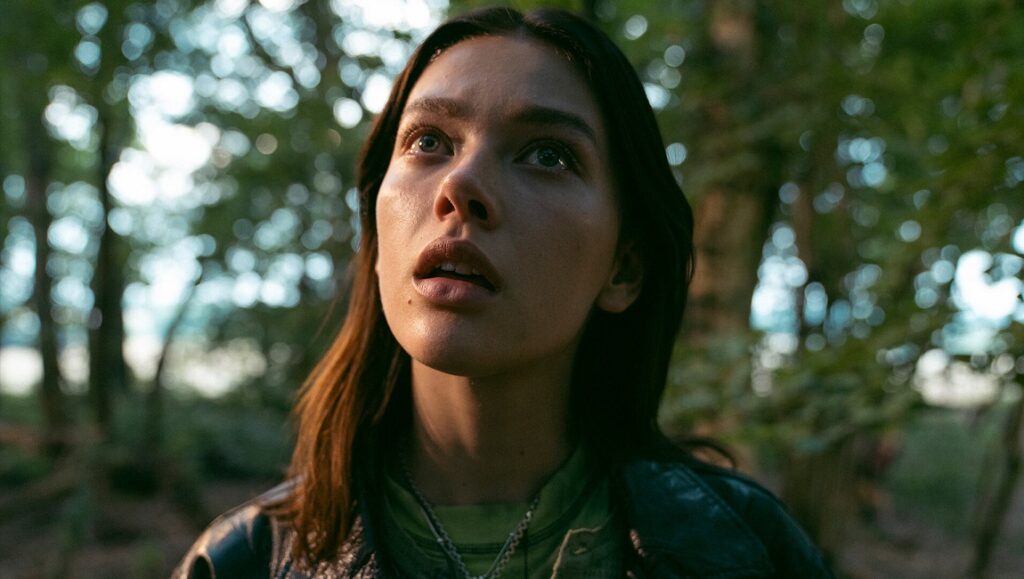 A Banquet movie still. Young woman looking up in the forest, with a concerned expression. Ruth Paxton film.