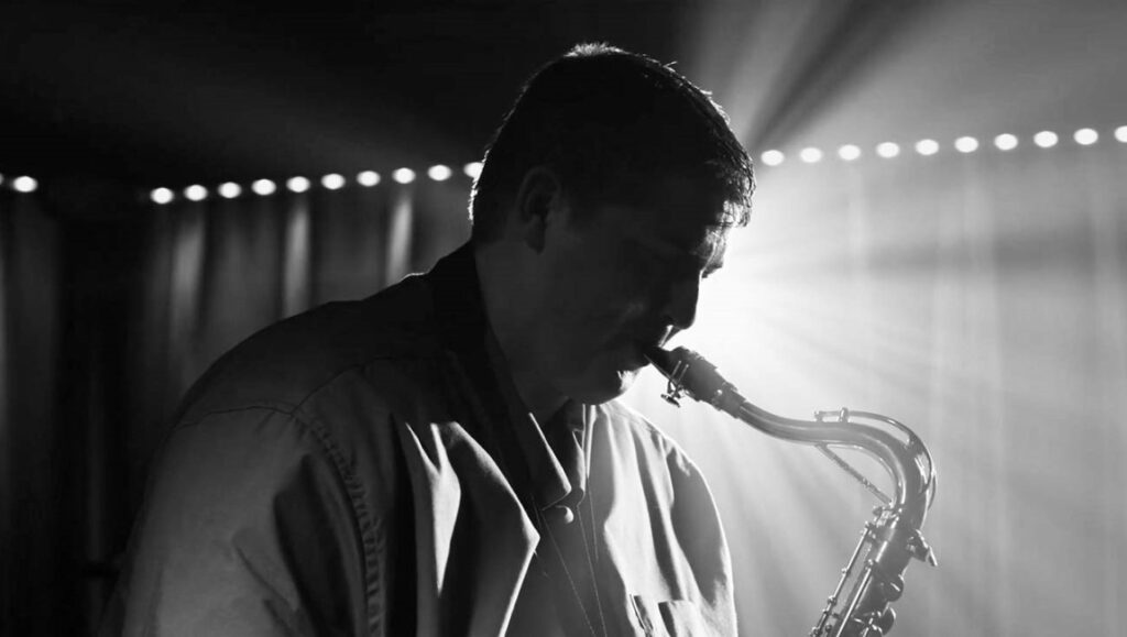 Butter — Paul A. Kaufman Black and white film still from Berlin Film Festival 2022: Musician plays saxophone.