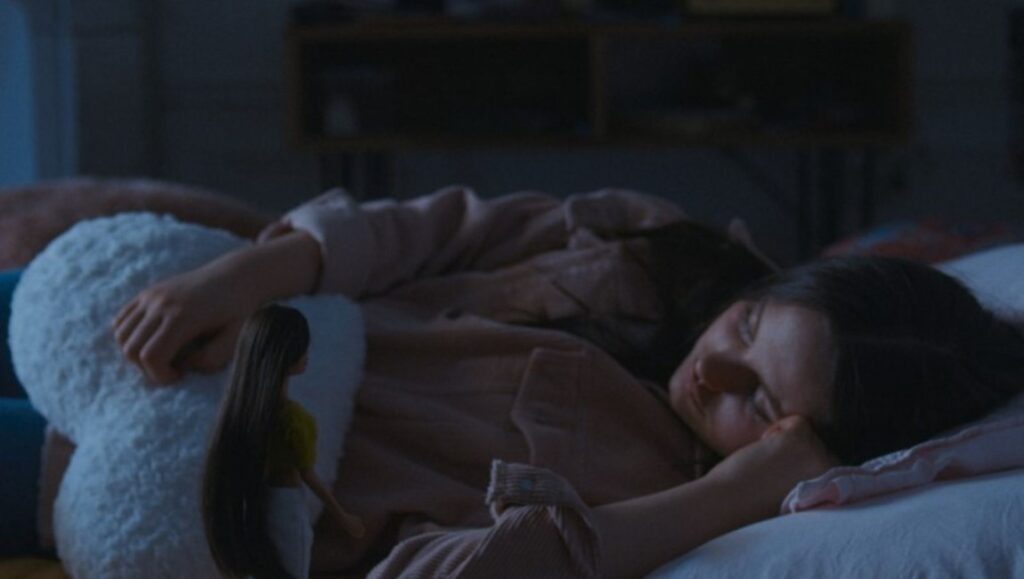 Coma film still from Berlin Film Festival 2022: A woman sleeps in bed hugging a large, white stuffed animal.