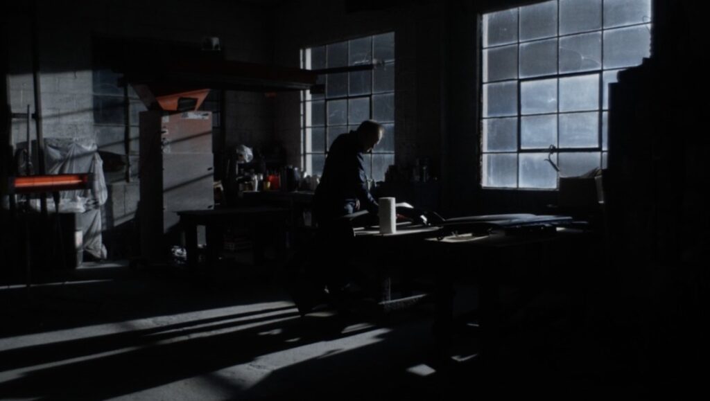 Happer's Comet film still, Berlin Film Festival 2022. Man works in a dimly lit workshop with large windows.