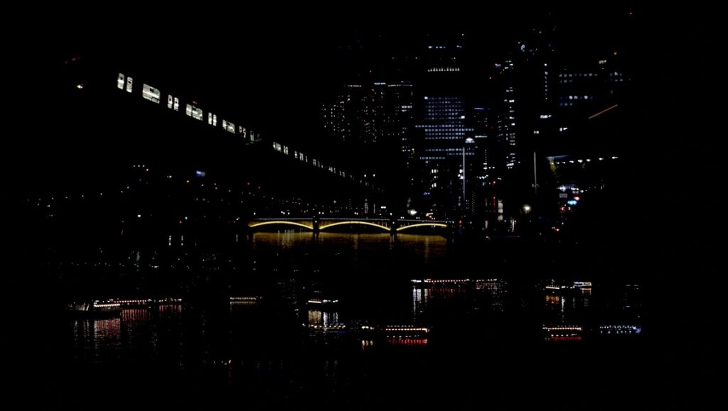 The Sower of Stars — Lois Patiño The Sower of Stars still: Night cityscape featuring a bridge, river reflections, and city lights.