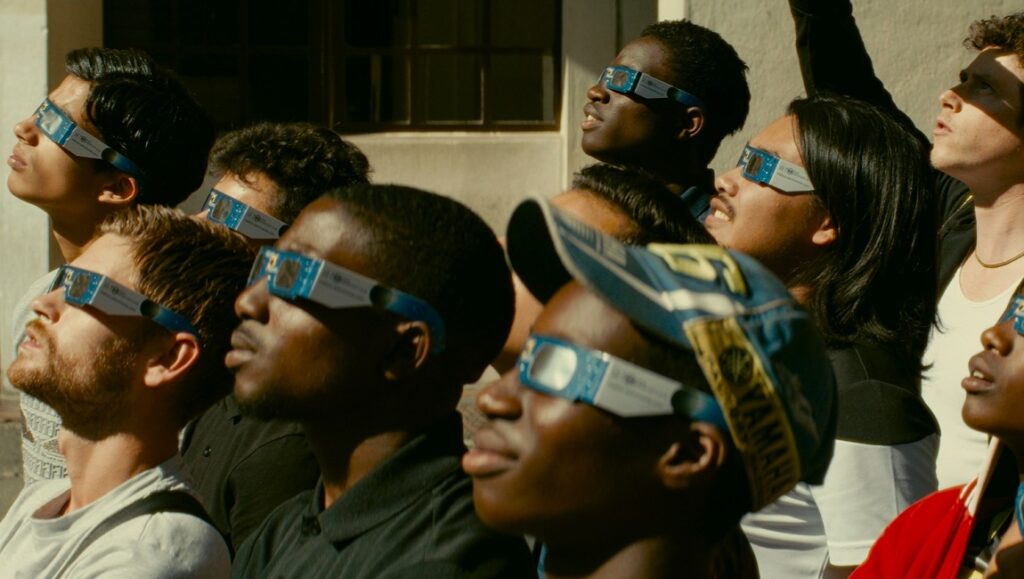 Gagarine — Fanny Liatard & Jérémy Trouilh Still from Gagarine movie. Group of young people wearing solar eclipse glasses, looking up.