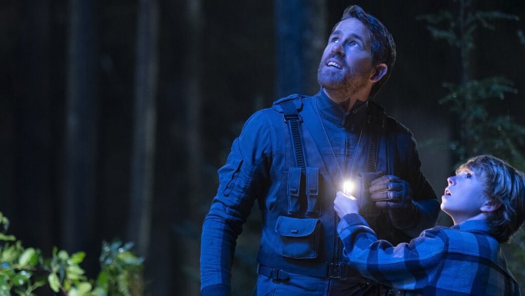 The Adam Project — Shawn Levy Ryan Reynolds and Walker Scobell in The Adam Project movie. Father and son looking up with a flashlight.