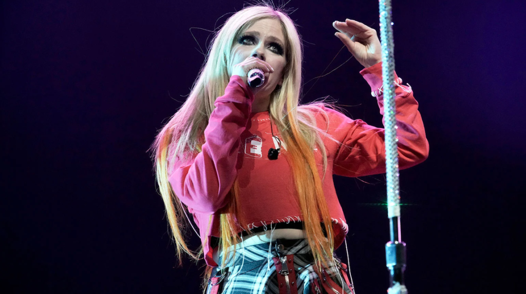 Avril Lavigne performing live in February 2022. The singer is wearing a red top and plaid skirt.