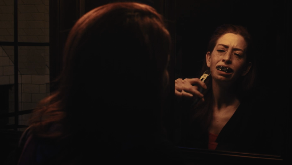 Sin Eater — Carmelo Chimera Sin Eater movie scene. Woman with bloody teeth reflected in mirror. March 2022 film review.